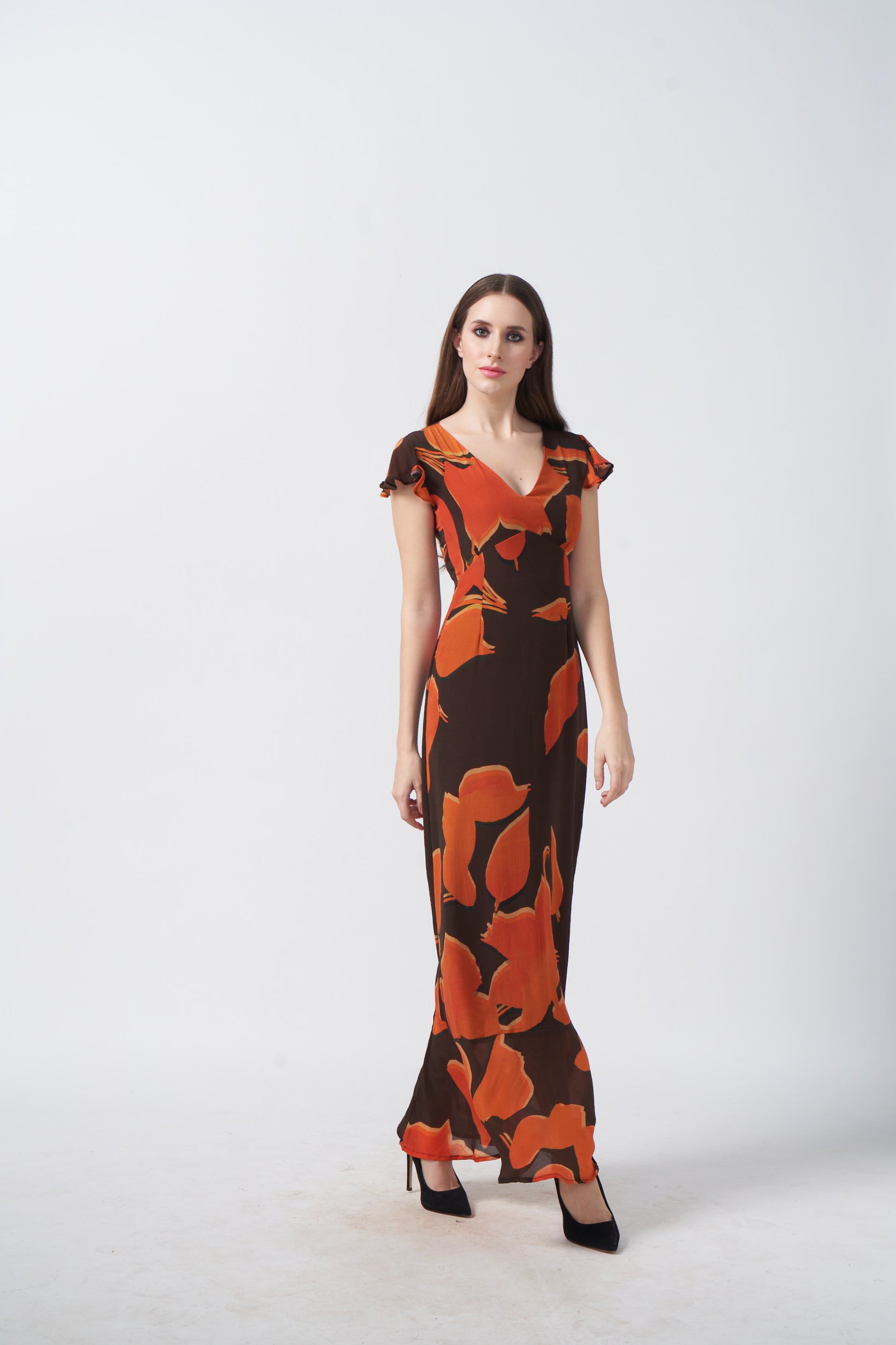 Model in front-facing pose wearing orange and brown abstract crepe dress with ruffle sleeves.