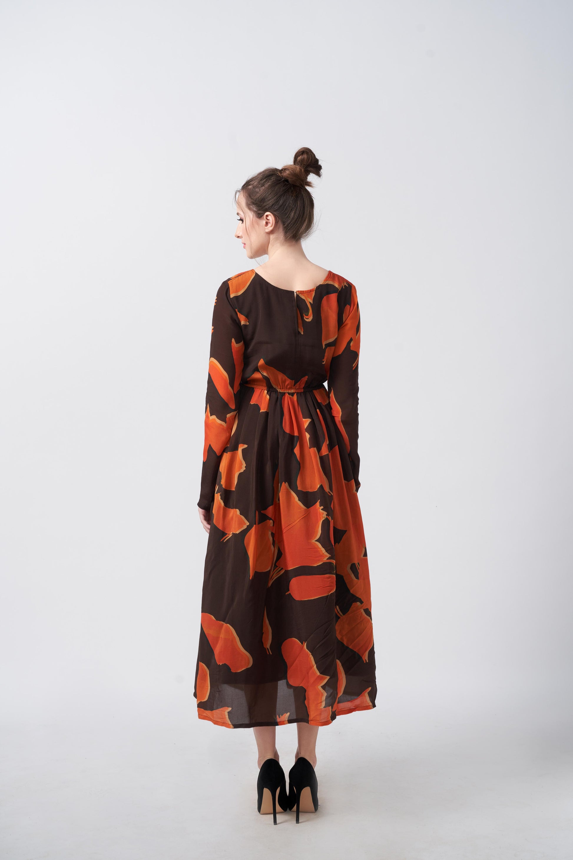 Back view of the model in an abstract midi dress with full sleeves and soft crepe flow.