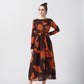 Front view of the model in an orange and brown crepe midi dress with round neckline and elegant knot detailing.