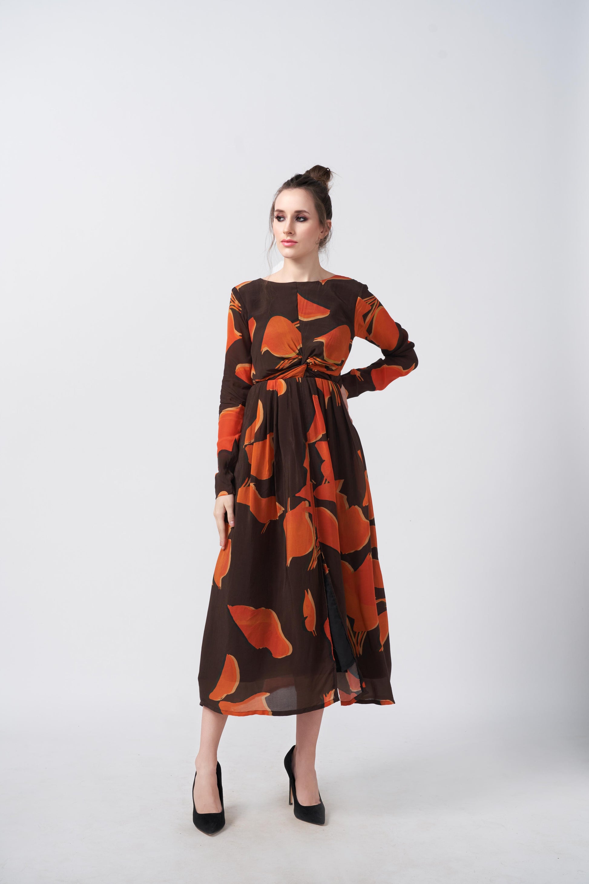 Front view of the model in an orange and brown crepe midi dress with round neckline and elegant knot detailing.