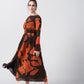 Model posing in an orange and brown abstract print midi dress with knot front detail and long sleeves, capturing movement and grace.