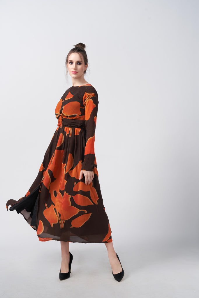 Model posing in an orange and brown abstract print midi dress with knot front detail and long sleeves, capturing movement and grace.