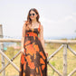 Model in sunglasses standing by a wooden railing in the orange and brown abstract dress, showcasing daytime styling.