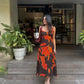 Model walking towards camera in orange and brown dress, captured in motion to show drape and movement.