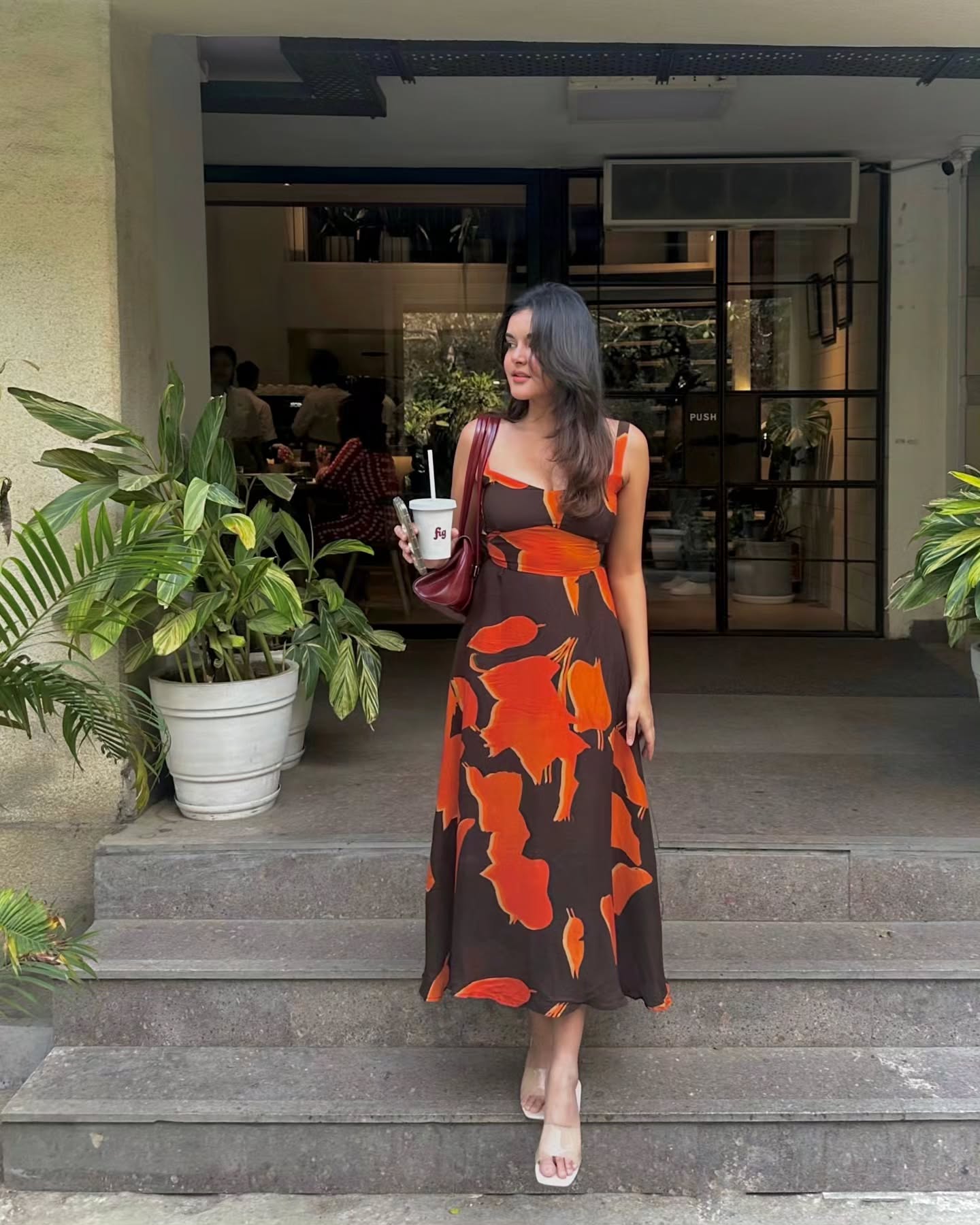 Model walking towards camera in orange and brown dress, captured in motion to show drape and movement.