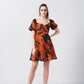 Model facing front in orange and brown abstract short dress with sweetheart neckline and puff sleeves.