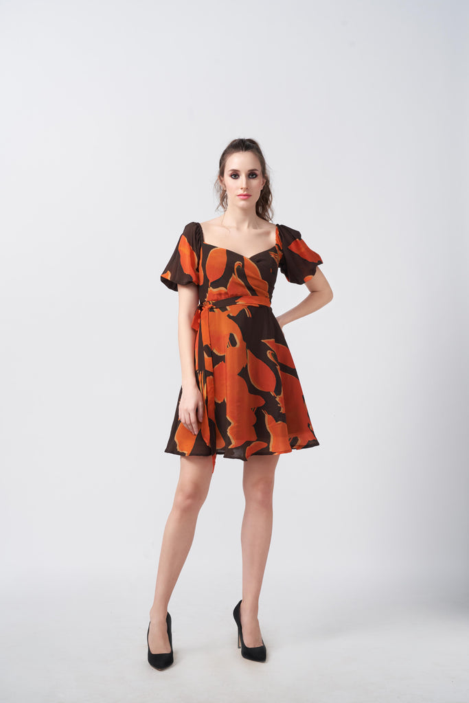 Model facing front in orange and brown abstract short dress with sweetheart neckline and puff sleeves.