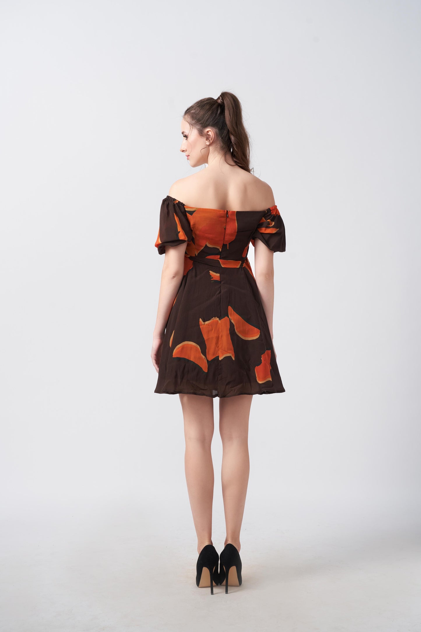back view of model in orange and brown abstract mini dress with puff sleeves. 