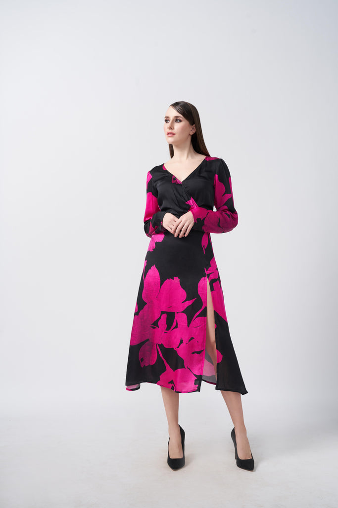 Model wearing a pink and black floral silk midi dress with V-neckline, long sleeves, and side slit, standing front-facing.