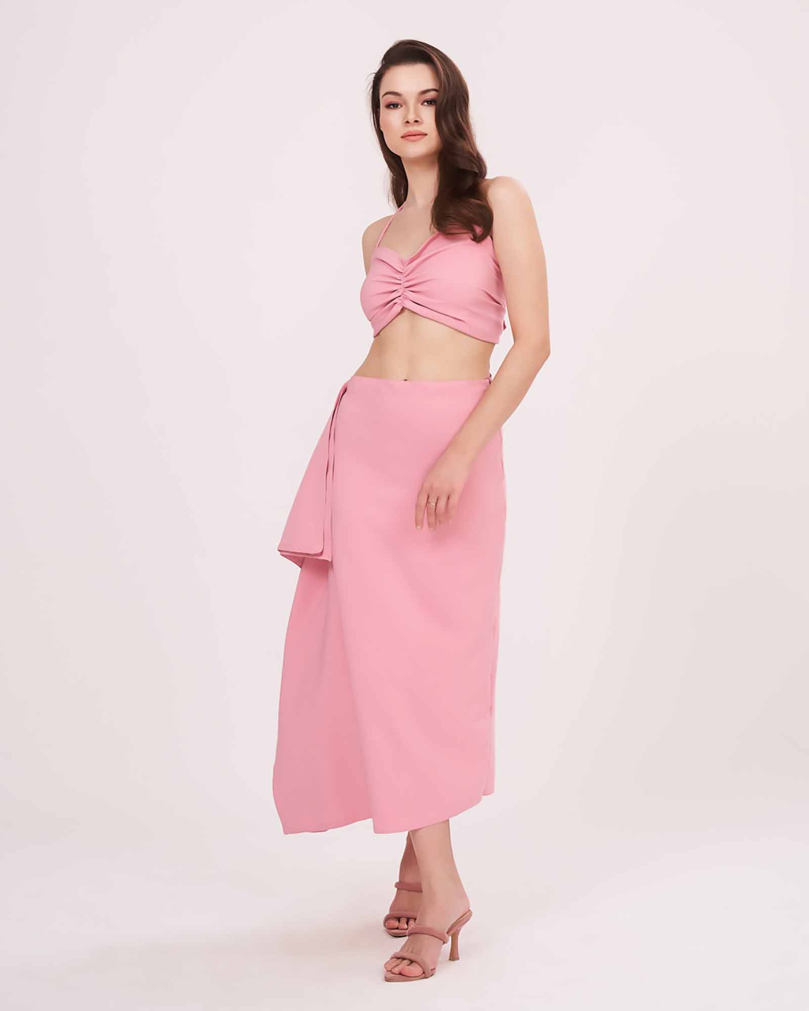 Model in a relaxed standing pose wearing the pink halter neck crop top and matching ruched skirt with side frill detail.