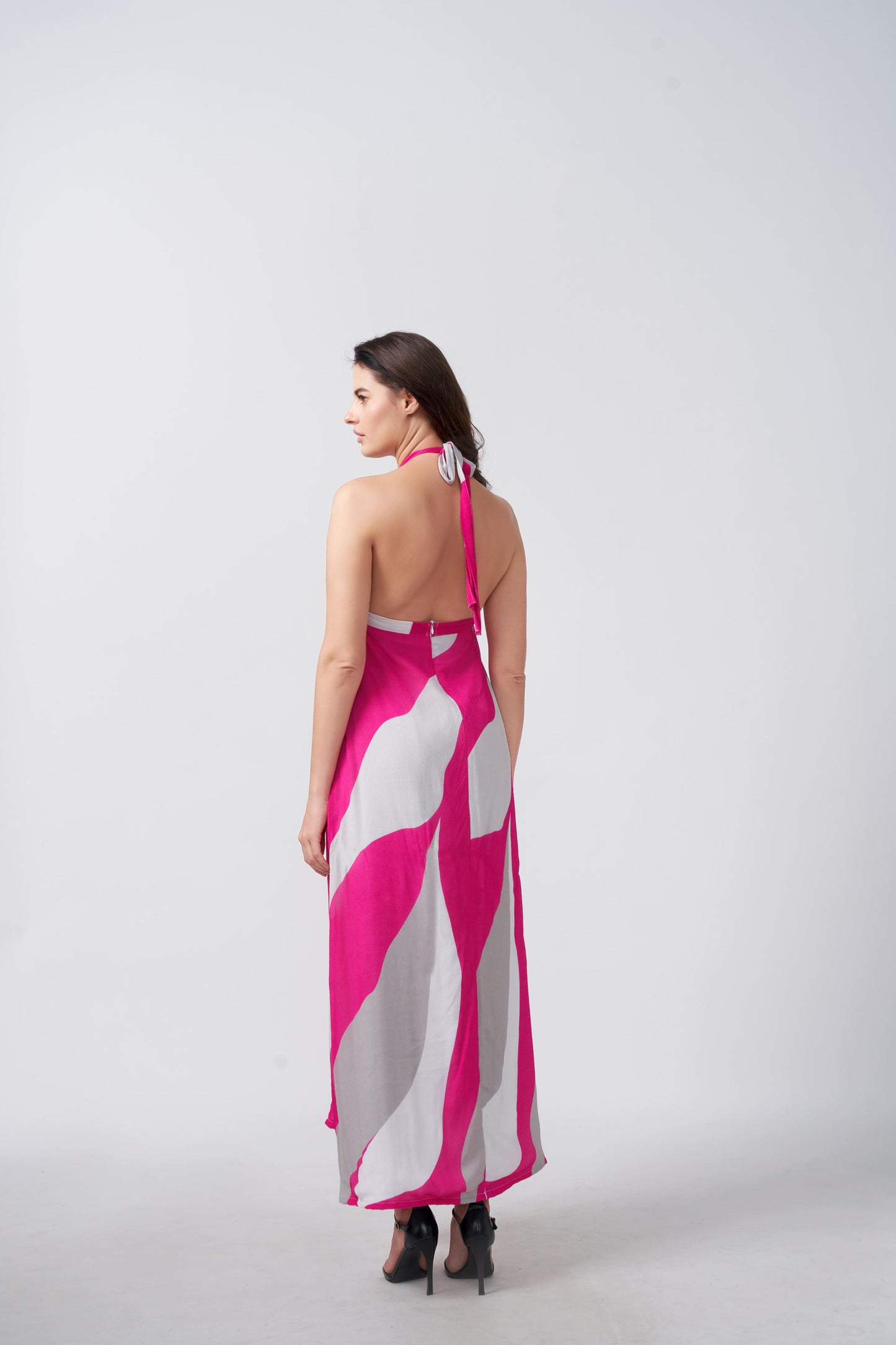 Back view of model in pink and grey halter maxi dress, featuring tie-up detail and fluid fabric fall.
