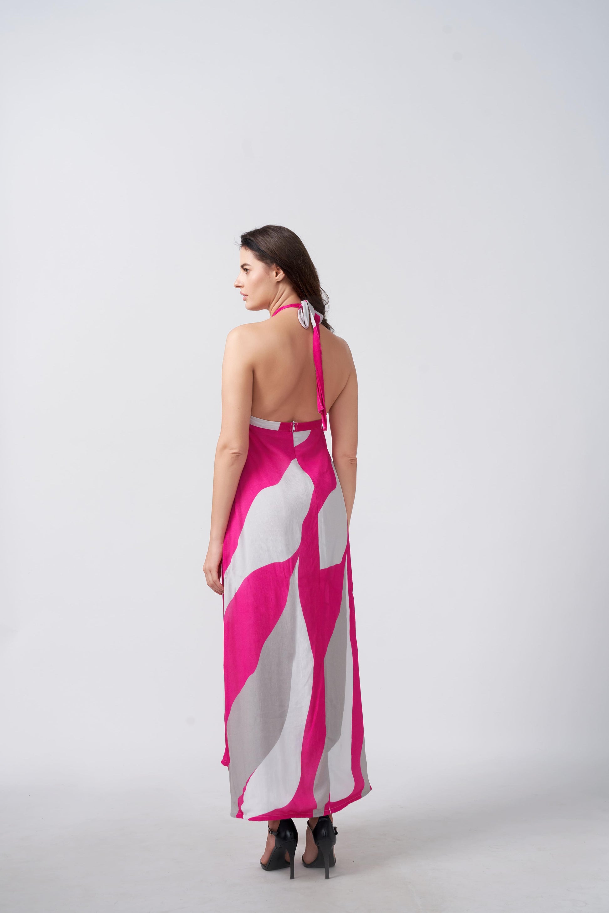 Back view of model in pink and grey halter maxi dress, featuring tie-up detail and fluid fabric fall.