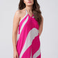 Model smiling in pink, grey, and white halter maxi dress, one hand near face, showing soft expression and style.