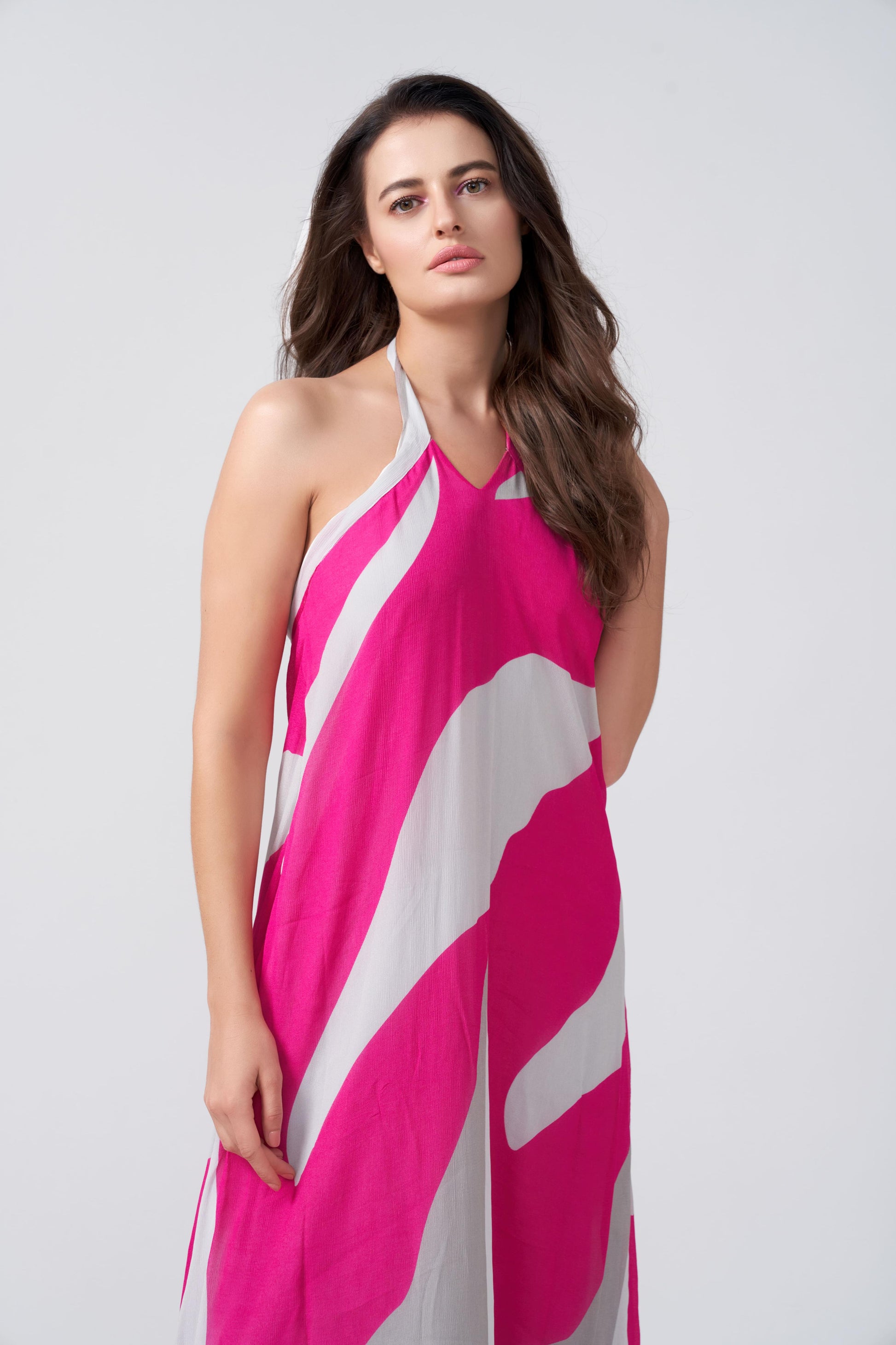 Model smiling in pink, grey, and white halter maxi dress, one hand near face, showing soft expression and style.