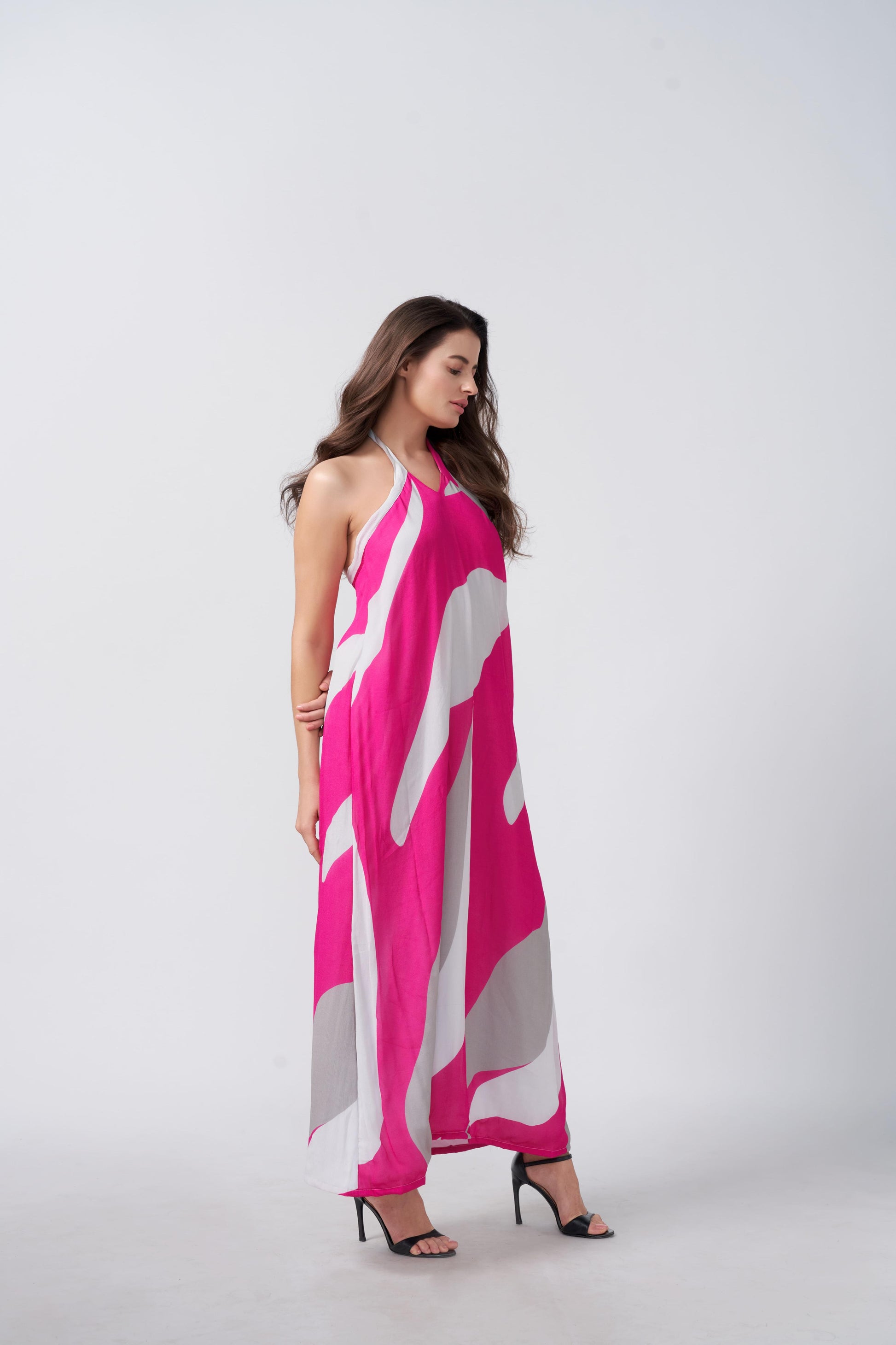 Side profile of model in pink, grey, and white abstract maxi dress, capturing the elegant drape and halter neckline.