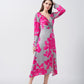 Model wearing a satin midi dress with pink floral print and full-length sleeves, posing with hand in hair against a grey background.