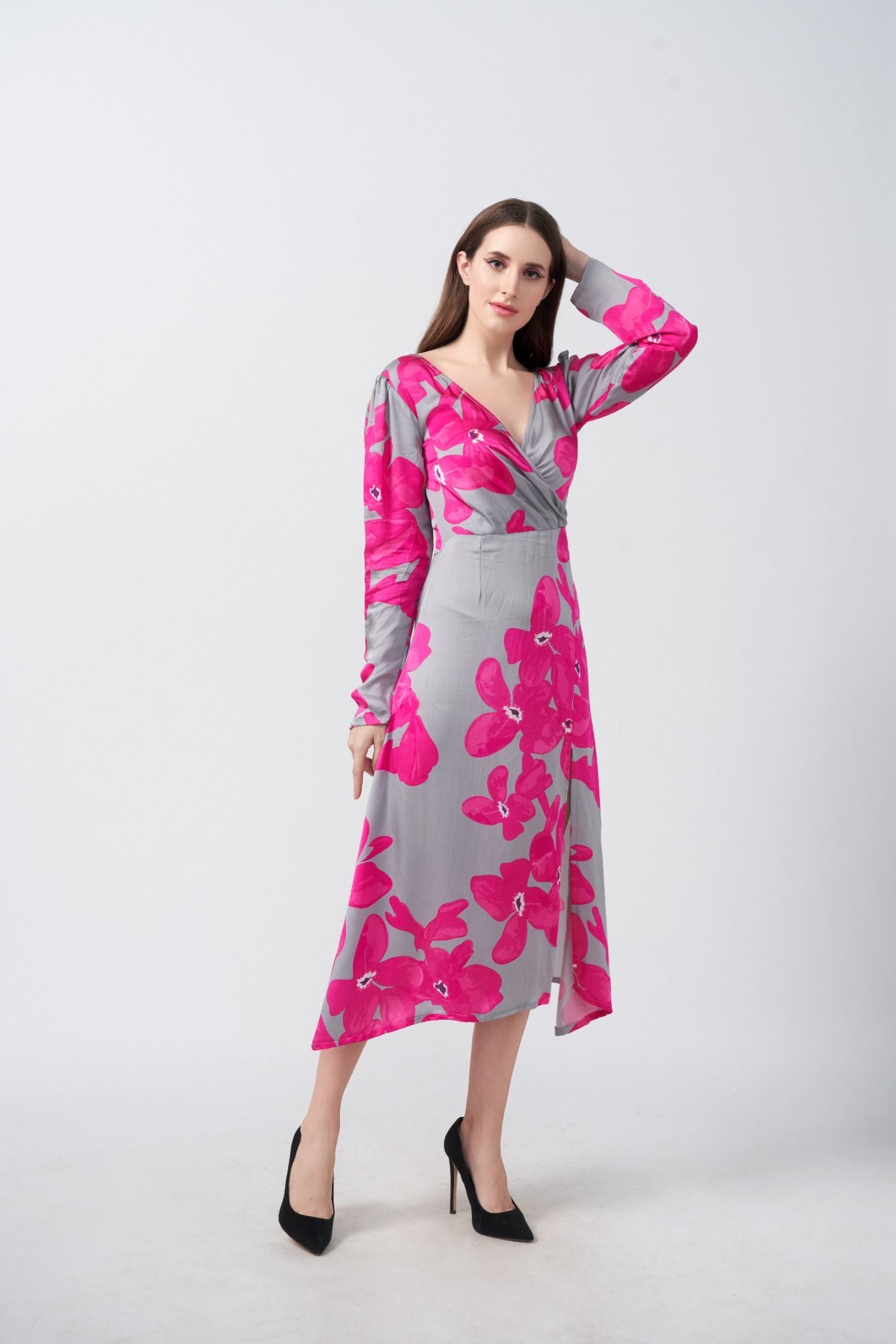 Model wearing a satin midi dress with pink floral print and full-length sleeves, posing with hand in hair against a grey background.