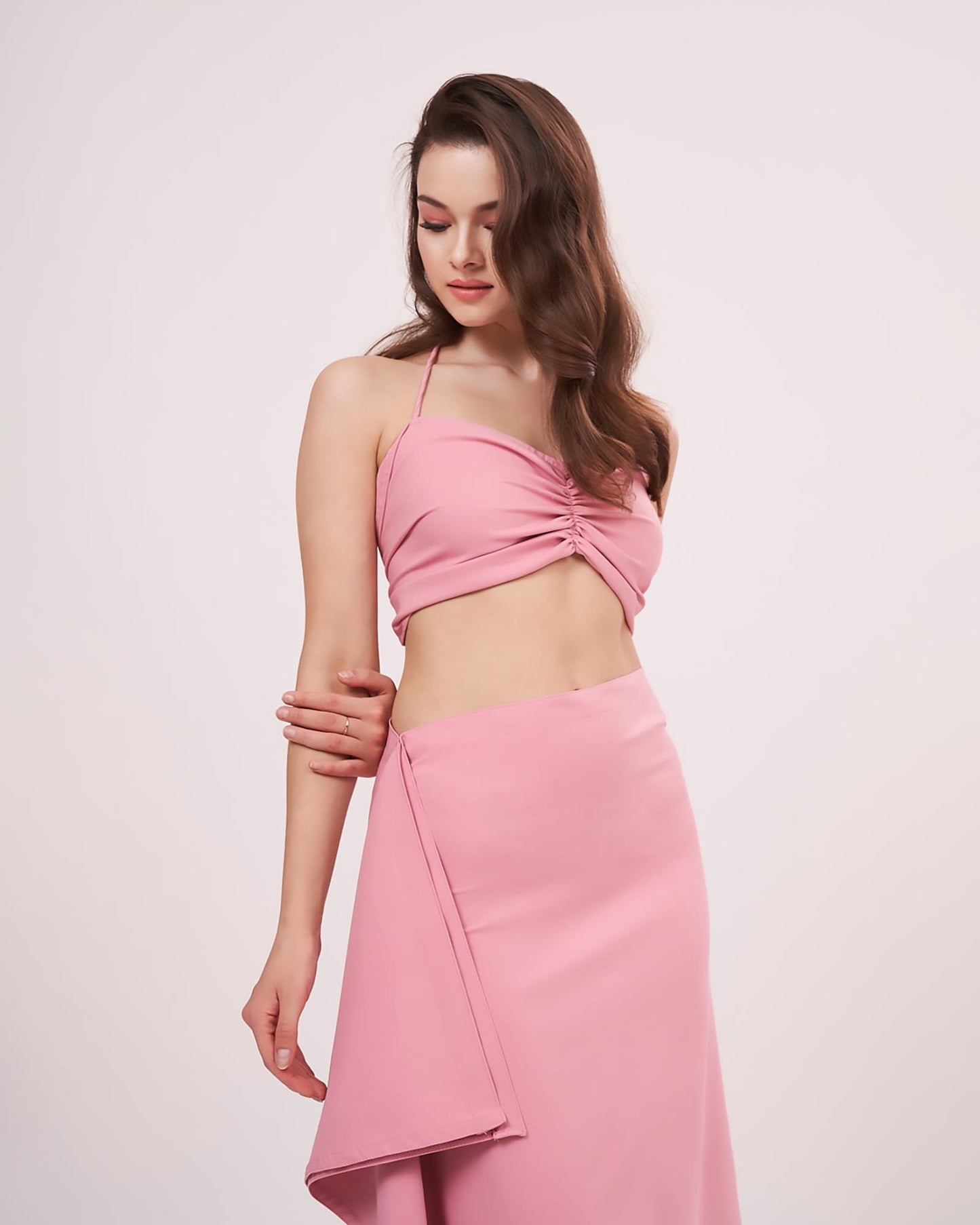 Model turned to a 3/4th profile, highlighting the ruched front and side frill flow of the solid pink co-ord skirt set.