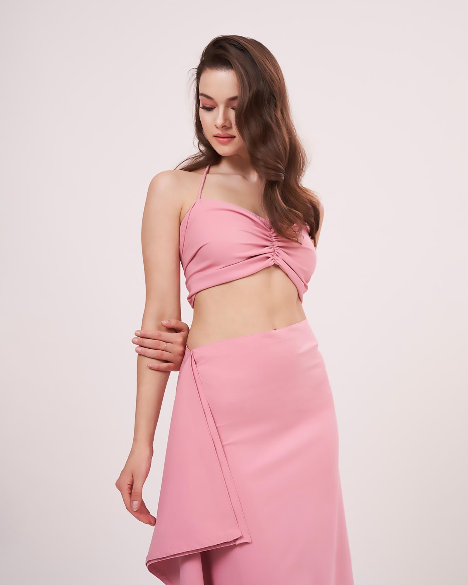 Model turned to a 3/4th profile, highlighting the ruched front and side frill flow of the solid pink co-ord skirt set.