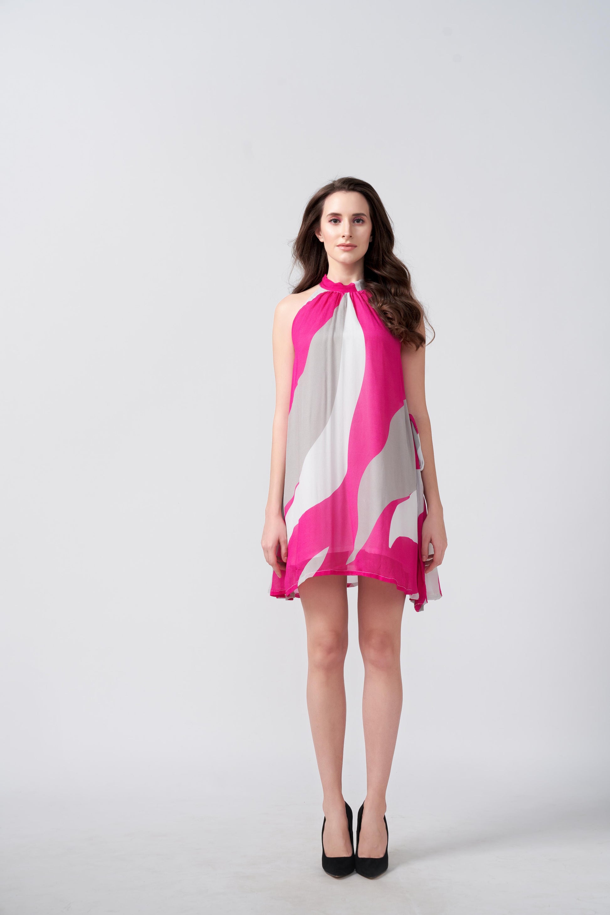 Model facing forward in a pink and white abstract chiffon dress with halter neckline and short hem.