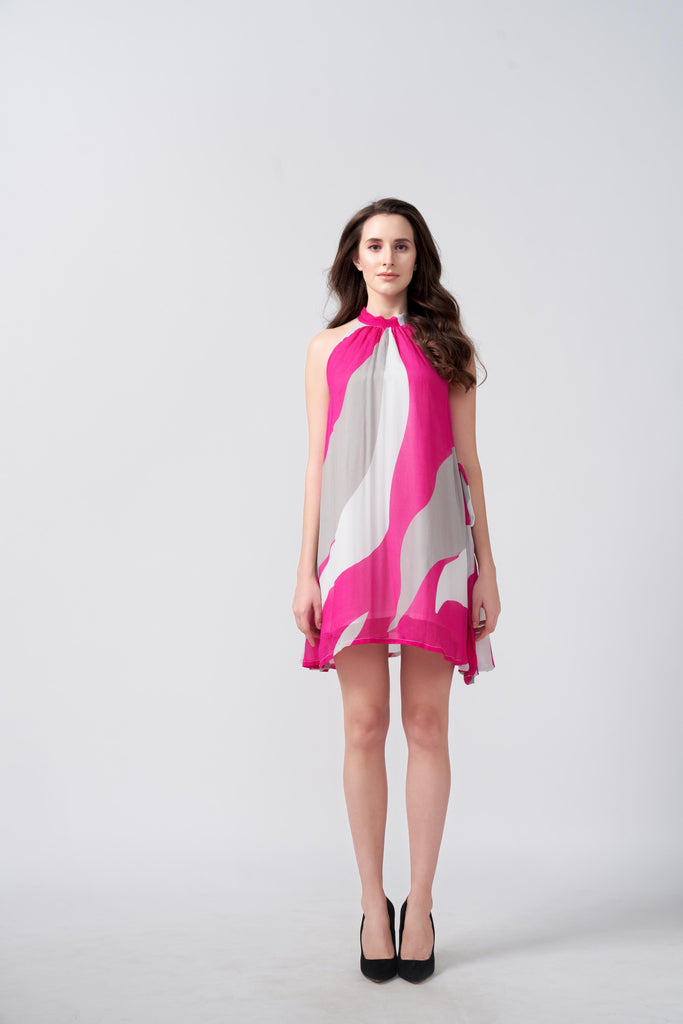 Model facing forward in a pink and white abstract chiffon dress with halter neckline and short hem.