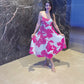 Midi-length dress featuring a vibrant hot pink floral print on a crisp white background, showcased in a lifestyle setting.