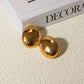 A pair of high-shine gold-toned stud earrings featuring a smooth, elongated oval shape with a gently domed surface.
