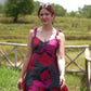 Video of a model posing in a red and pink abstract floral short dress with hands on hips, standing in an open field.