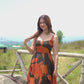 Video of a model in outdoor setting posing by a railing in the orange and brown midi dress, highlighting its relaxed fit.
