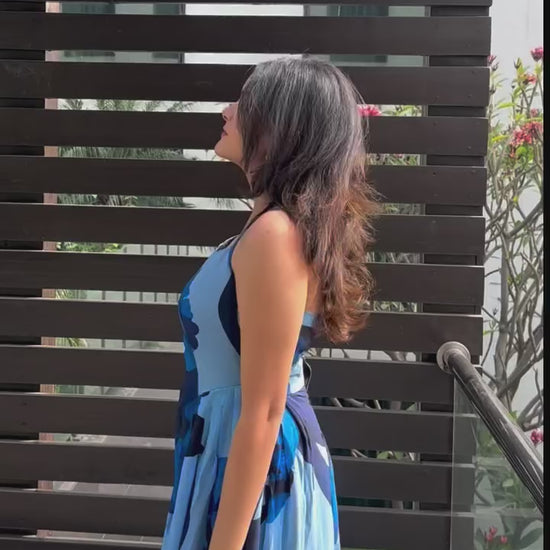 video of a model in halter neck blue floral crepe dress, highlighting the tie-back detail and flowy fabric.