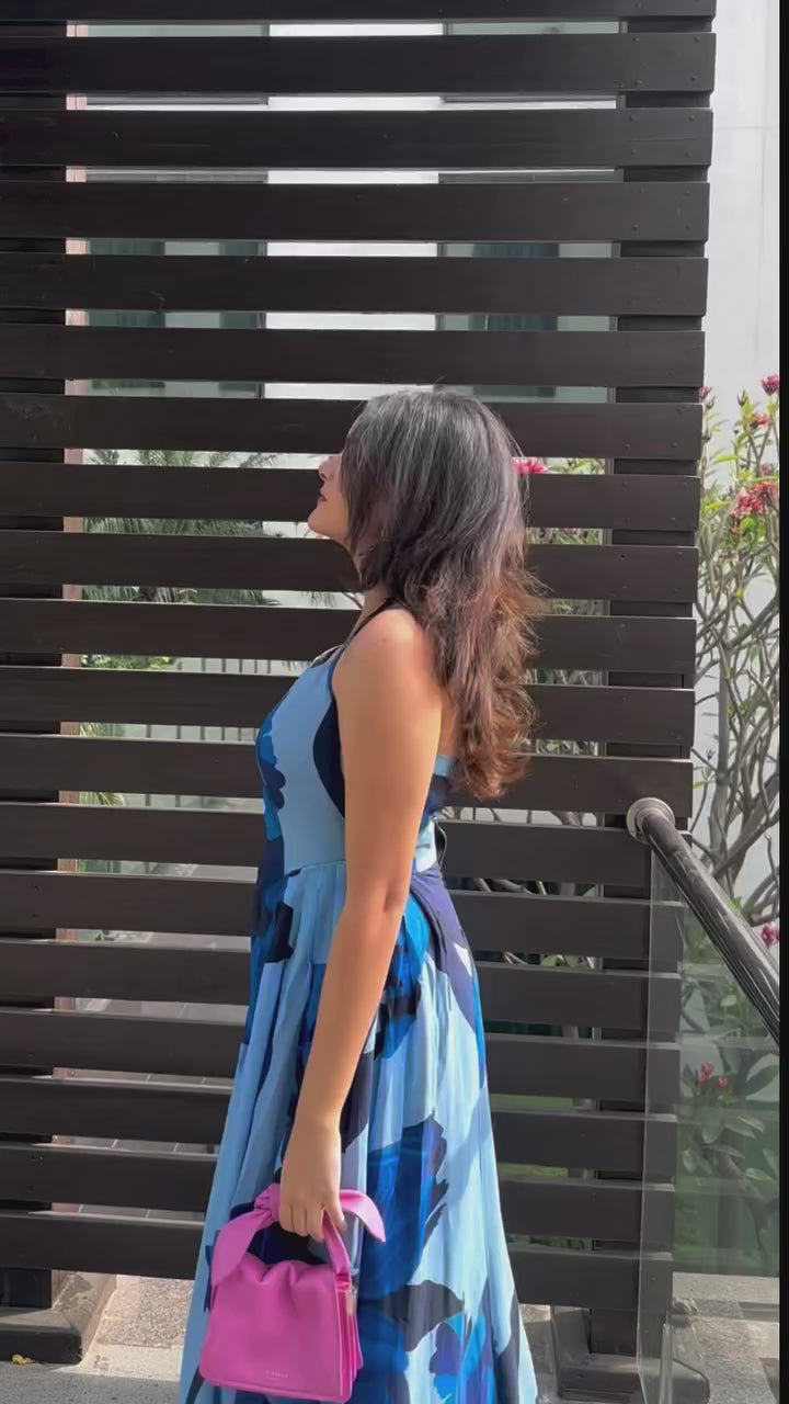 video of a model in halter neck blue floral crepe dress, highlighting the tie-back detail and flowy fabric.