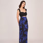 Model in a purple and black floral printed ankle-length dress with sweetheart neckline and strap shoulders, standing with arms relaxed.