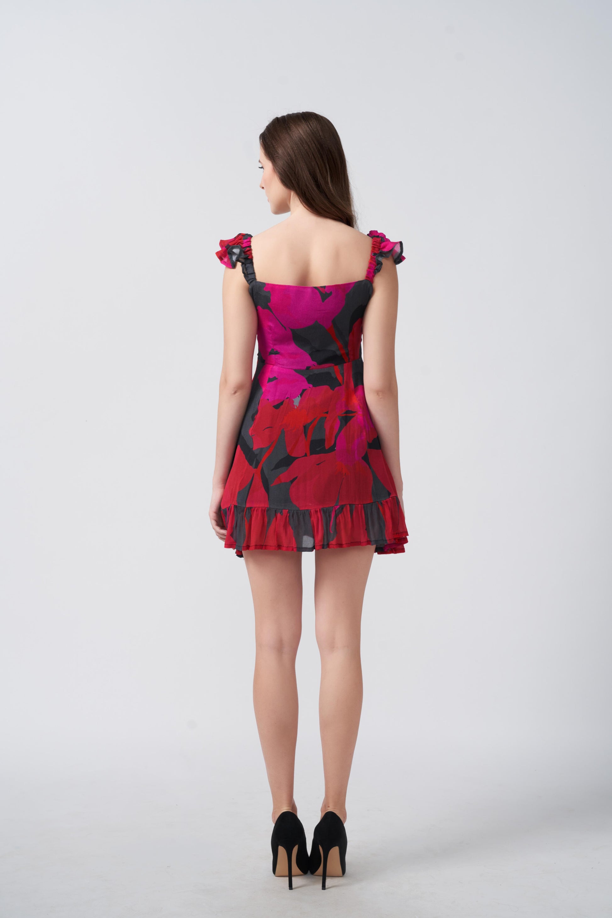 Back view of red and pink abstract floral short dress showing frill straps and fitted waist.