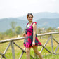 side profile of model wearing red and pink short floral dress, showing frill strap detail and walking in a field
