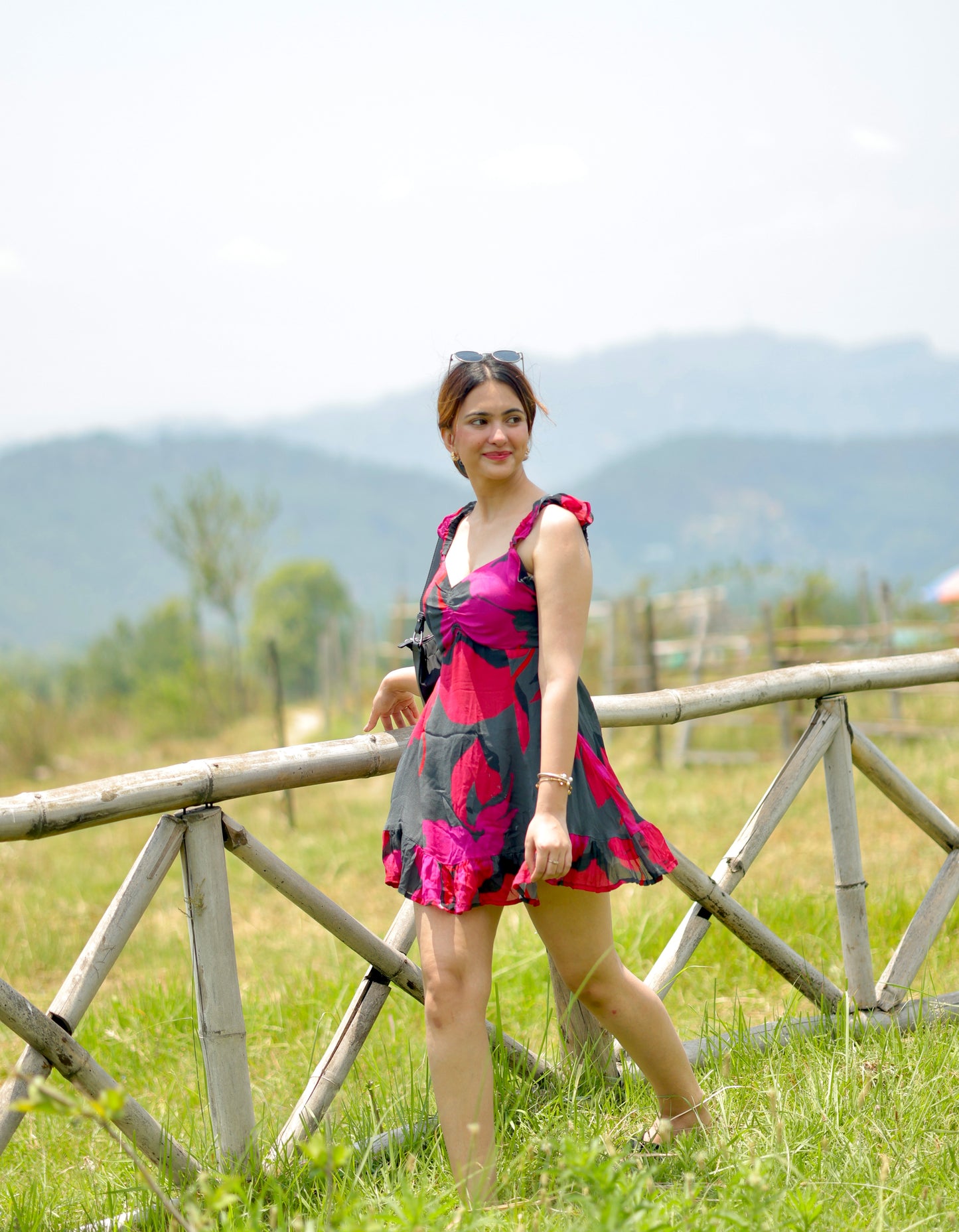 side profile of model wearing red and pink short floral dress, showing frill strap detail and walking in a field
