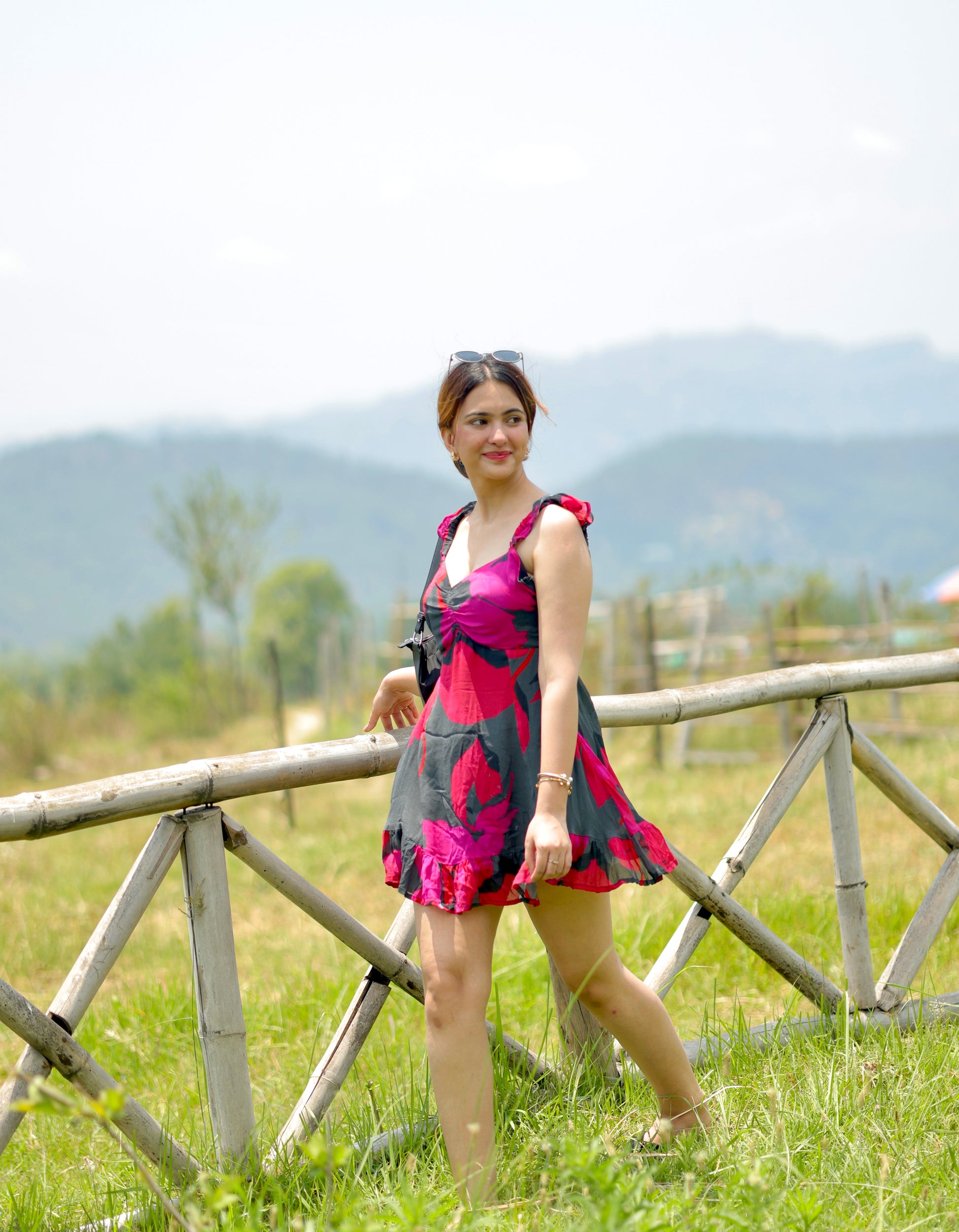 side profile of model wearing red and pink short floral dress, showing frill strap detail and walking in a field
