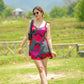 Model posing in a red and pink short floral dress with sweetheart neckline and frill straps, in a grassy field.