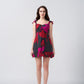 Model wearing a short red and pink abstract floral dress with frill shoulder straps, standing against a plain background.