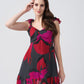 Model posing with hand in hair, wearing short red and pink floral dress with playful frill strap design.