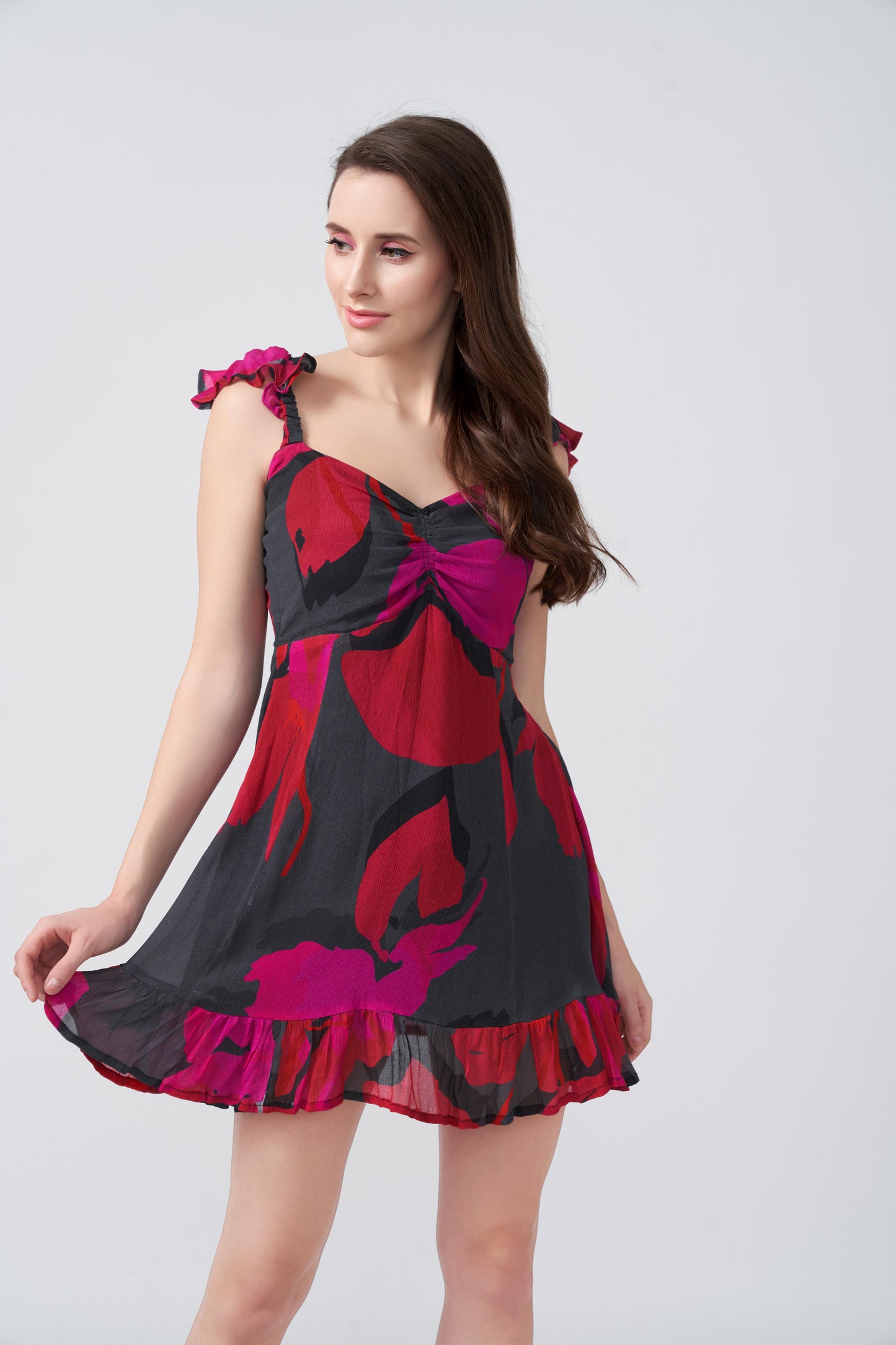 Side view of model posing outdoors in red and pink floral abstract dress with frill shoulder strap.