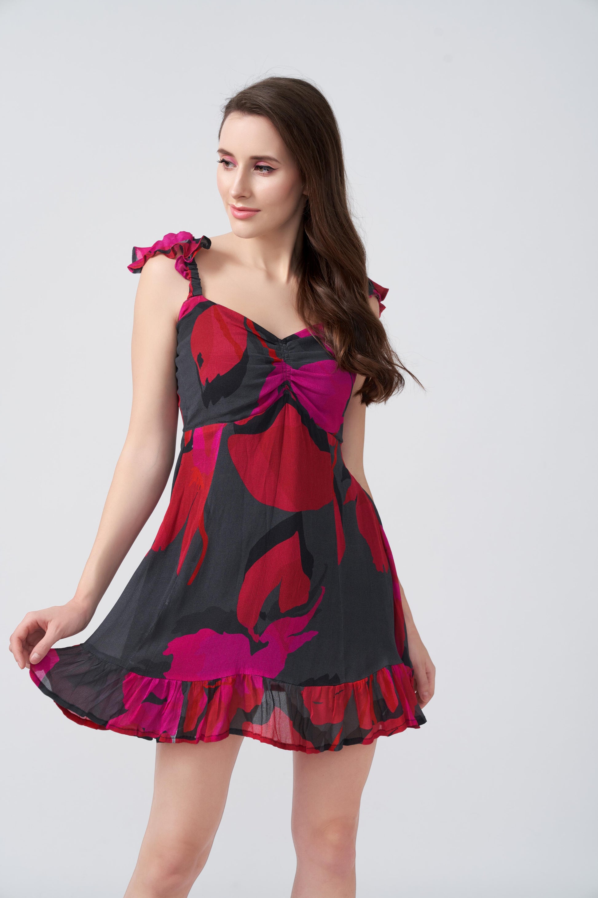 Side view of model posing outdoors in red and pink floral abstract dress with frill shoulder strap.
