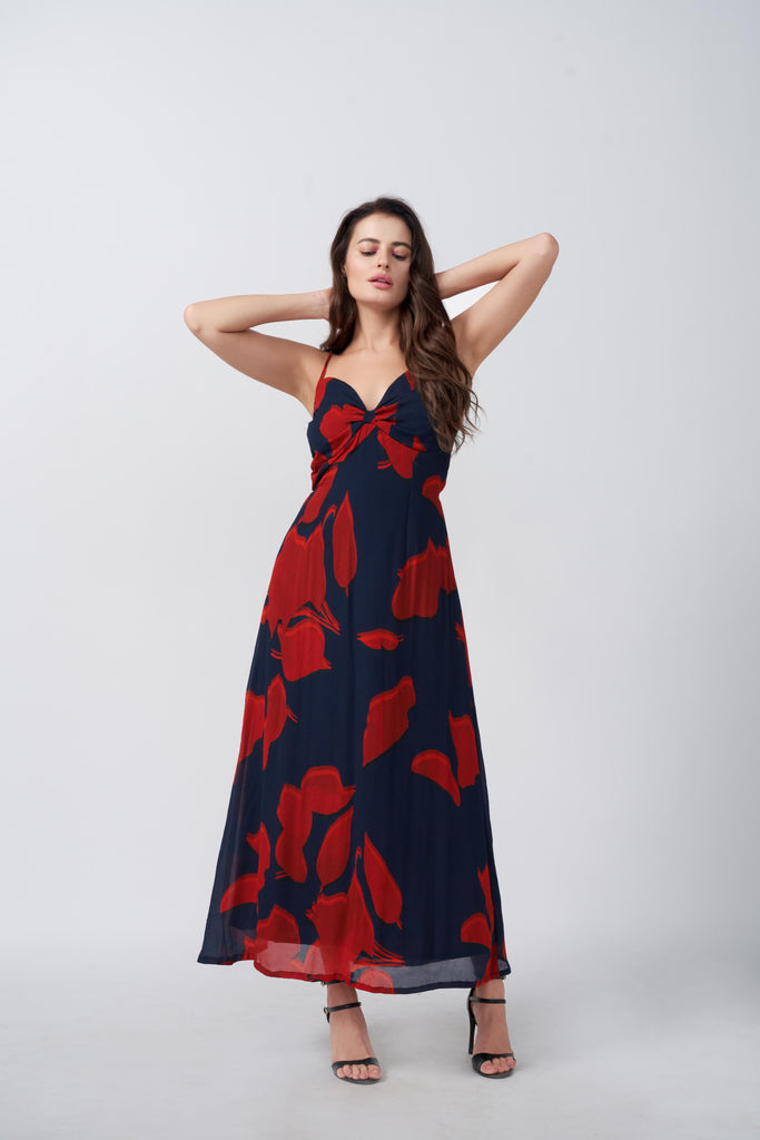 Model in red and blue floral ankle-length dress with spaghetti straps, arms raised in a relaxed pose.