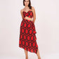 Model facing forward with both hands at her back, showcasing the red bralette top and high-waisted printed skirt with slit.