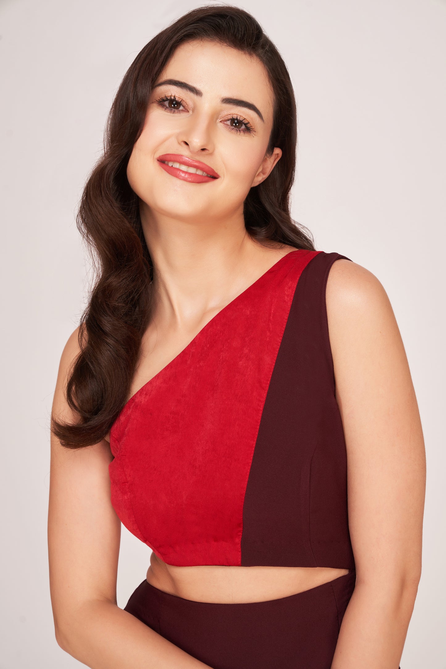 Mid-shot of the model smiling in a red and brown one-shoulder dress, highlighting the neckline and waist cut-out.