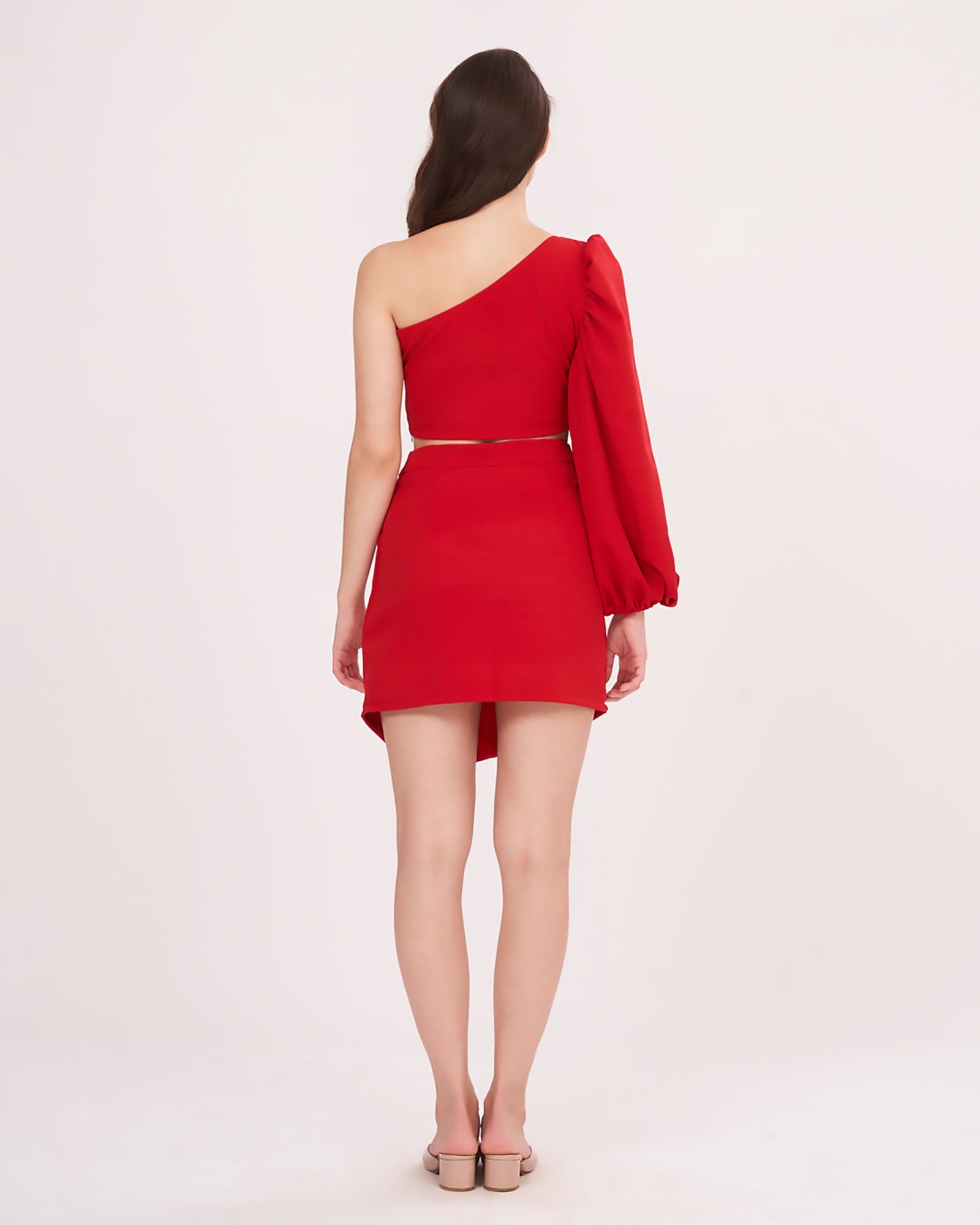 Rear view of the outfit with model standing relaxed, showcasing the back fit of the off-shoulder top and the mini skirt's tailored closure