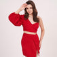 Zoomed-in view of model with hand near her hair, highlighting the sweetheart neckline and dramatic one-shoulder balloon sleeve of the red top.