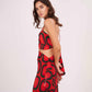 Side-facing pose showing the tie-up detailing on the back of the red halter crop top with flared printed skirt.