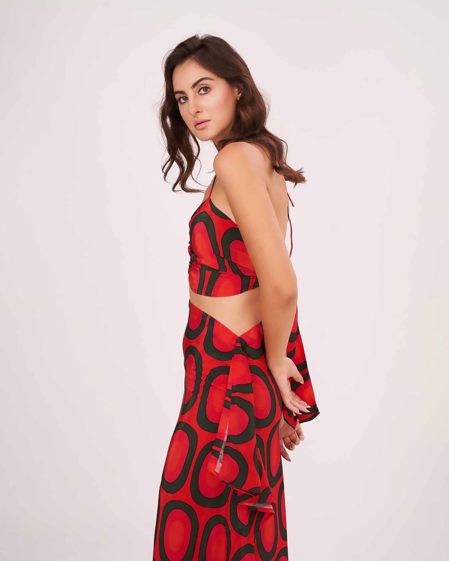 Side-facing pose showing the tie-up detailing on the back of the red halter crop top with flared printed skirt.