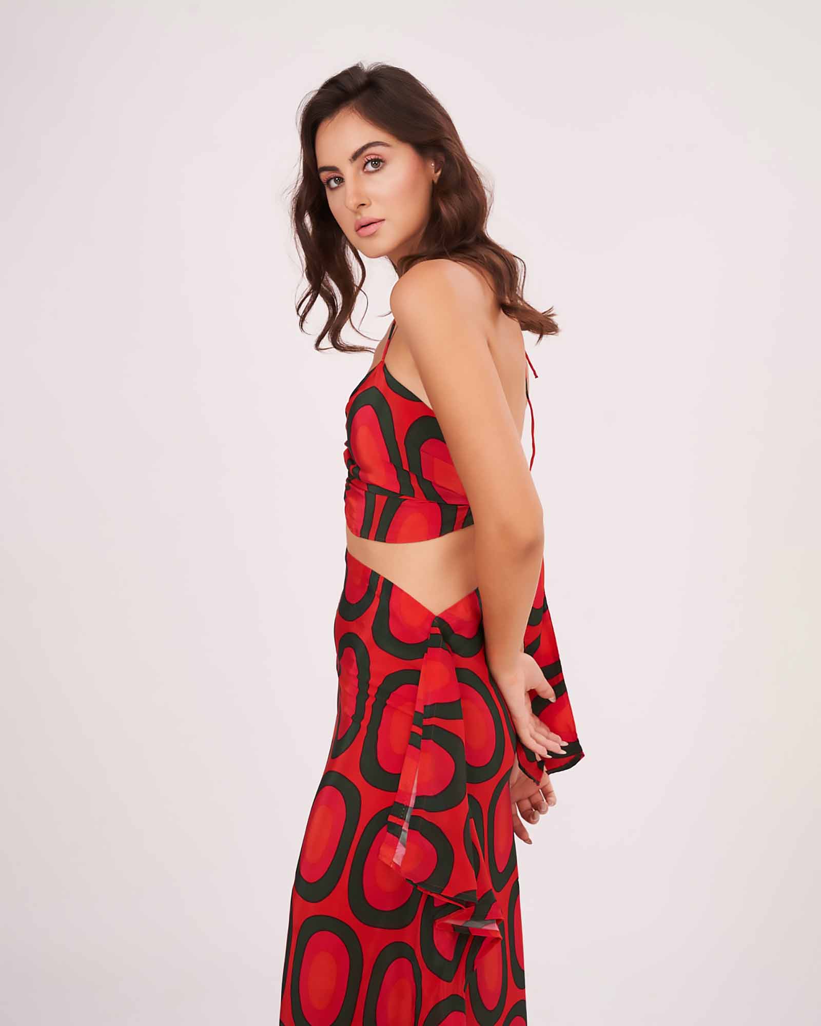 Side-facing pose showing the tie-up detailing on the back of the red halter crop top with flared printed skirt.