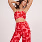 Model in red printed tube top and palazzo set posing with both hands up, showcasing the fitted bust and breezy pants in a playful pose.